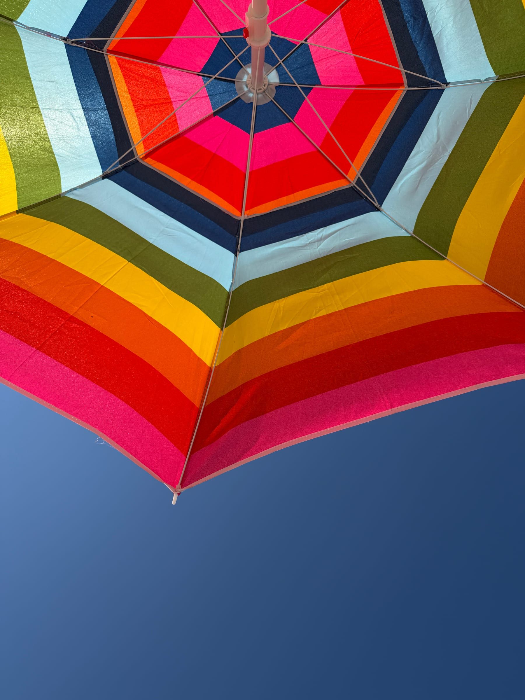 Kolorowy parasol plażowy widziany od spodu na tle błękitnego nieba
